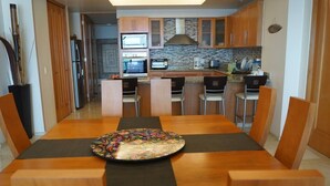 A modern kitchen with wooden cabinets, a central island, and a dining table with chairs. - CONDO SHAGUI BY TRVL2HM (Puerto Vallarta)