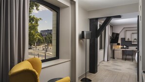 Een moderne hotelkamer met een groot raam, een gele fauteuil, een vloerlamp en uitzicht op de stad.