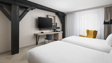 Ein Hotelzimmer mit einem großen Bett, einem Schreibtisch mit Fernseher, einem Sessel und einem Fenster mit Vorhängen.