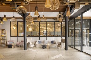 A modern interior with a seating area, large windows, and hanging pendant lights. - Hilton Garden Inn Paris La Villette (Paris)