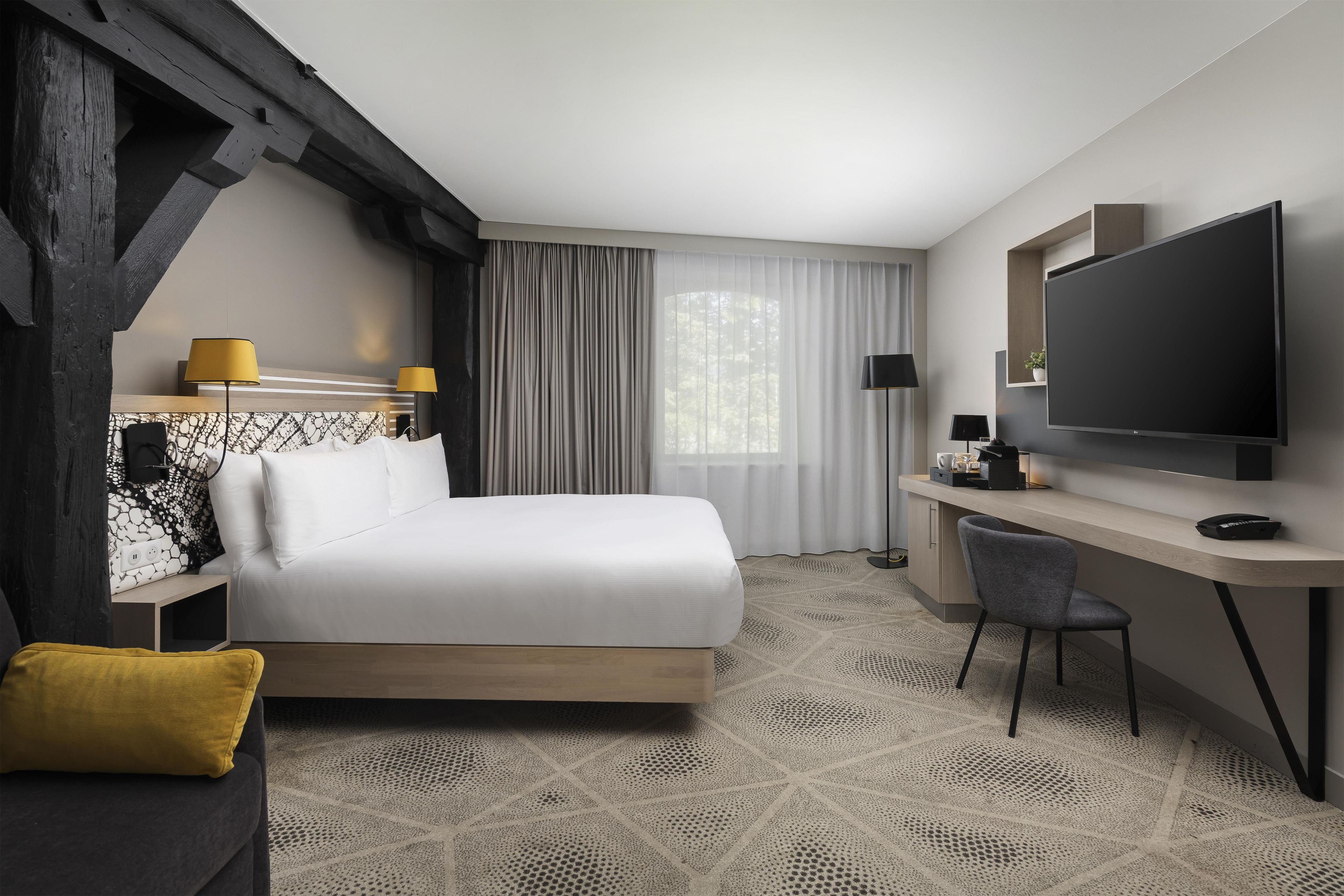 A hotel room with a bed, a desk, a chair, a television, and a window with curtains.