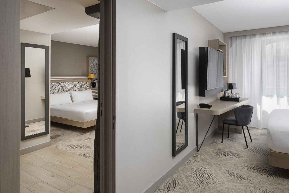 A hotel room with a bed, a desk, a chair, a TV, and a large mirror.