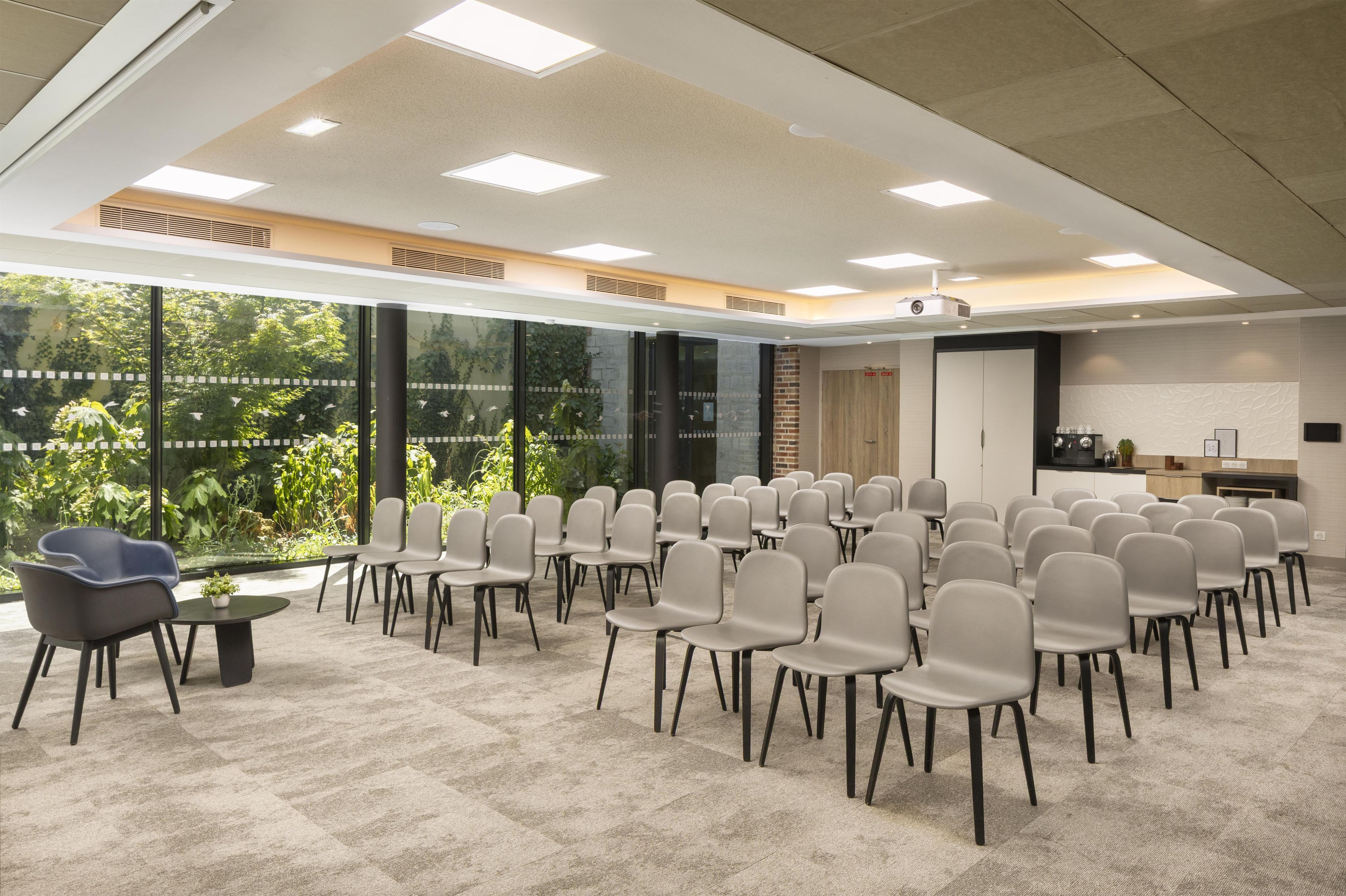 A conference room with rows of chairs, a projector, and a large window with a view of greenery.