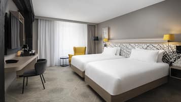 Habitación de hotel con dos camas, un escritorio, una silla, una mesita y una lámpara.