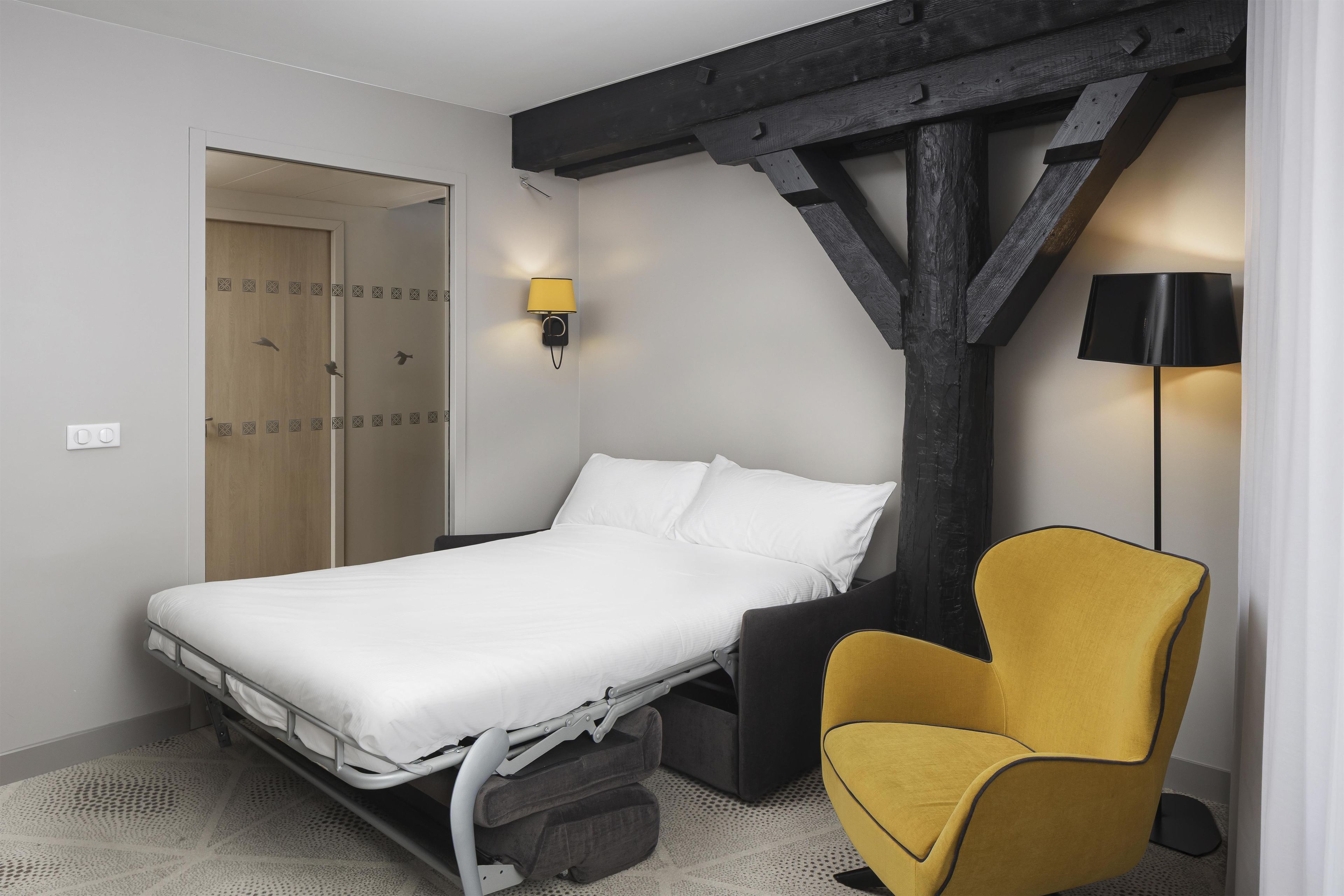 Un dormitorio con una cama, una silla y una lámpara de pared.