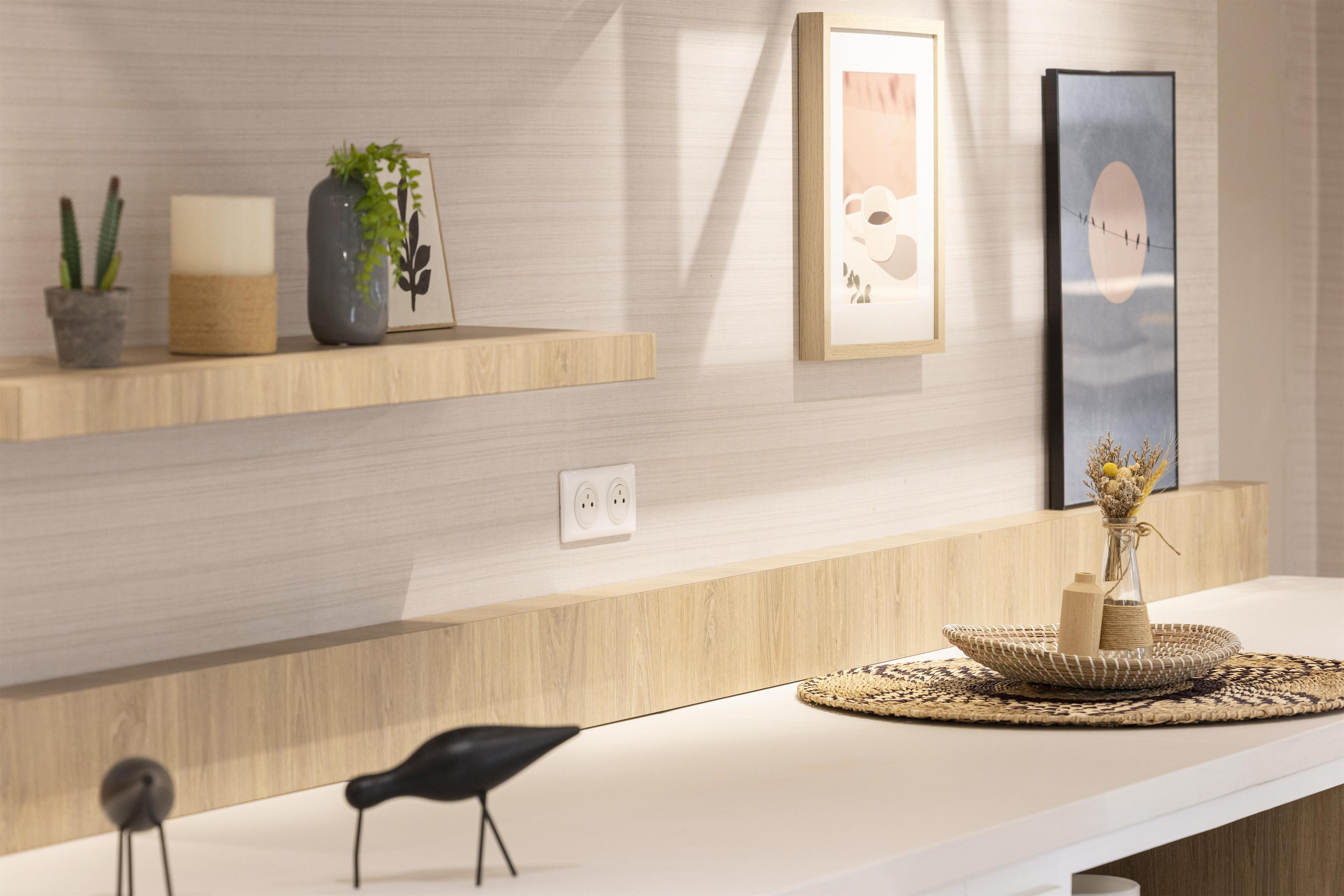 A modern reception area with a white counter, a black chair, and decorative items including a vase with dried flowers, a framed picture, and a small potted plant.