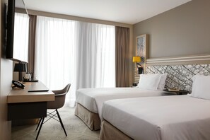 A hotel room with two beds, a desk with a chair, a TV, and a lamp. - Hilton Garden Inn Paris La Villette (Paris)