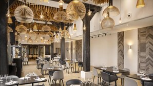 Een modern restaurantinterieur met meerdere eettafels, zwarte stoelen en bijzondere hangende lampen.