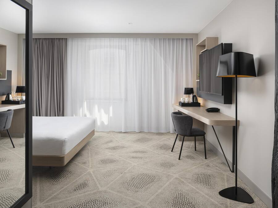 A modern hotel room with a bed, desk, chair, and a large mirror.