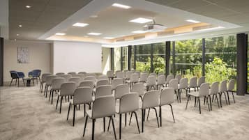 A conference room with rows of chairs, large windows, and a carpeted floor.