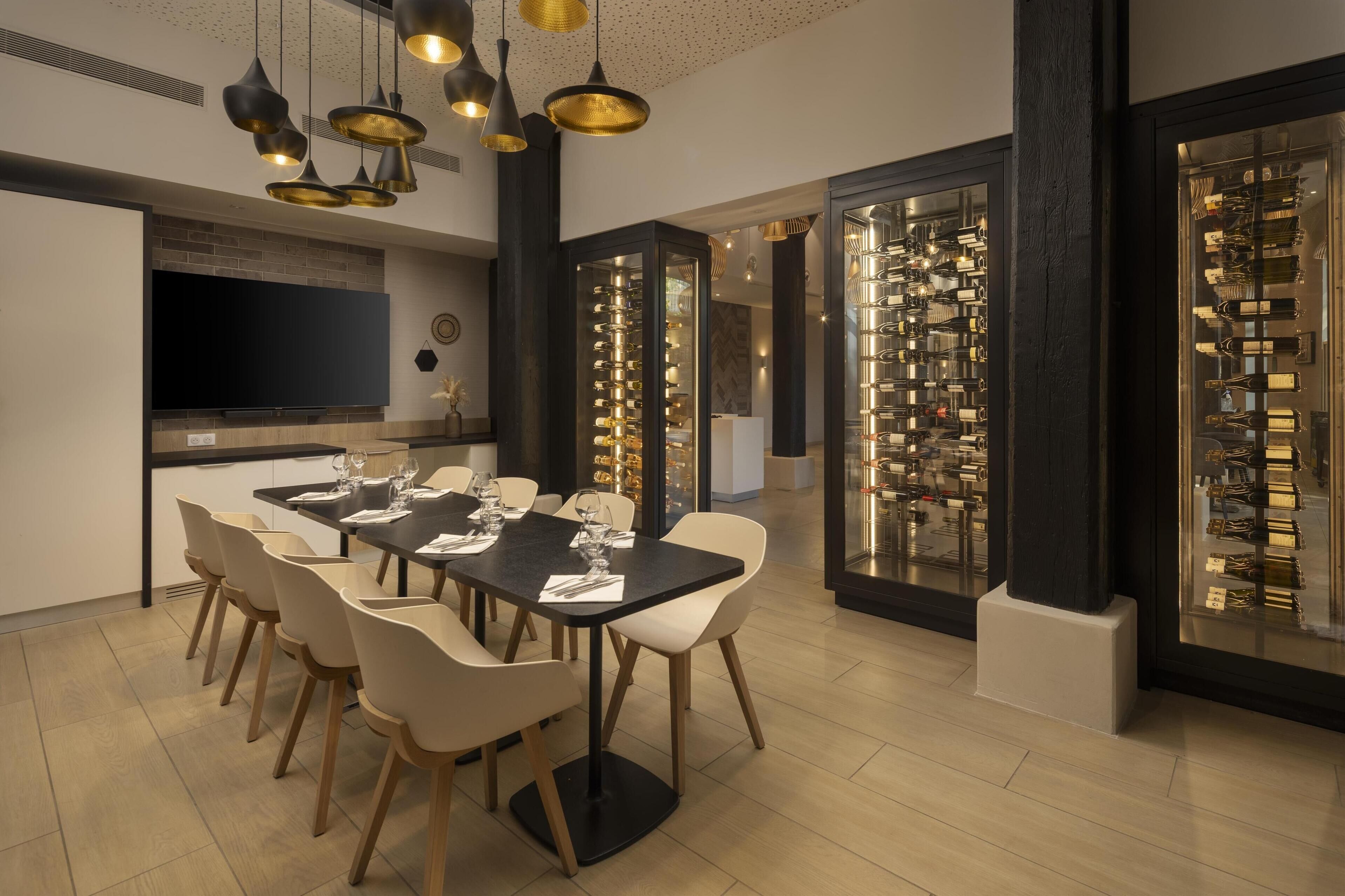 A modern dining area with a long table, white chairs, and a black tablecloth. There is a television on the wall and a display of items on the right.