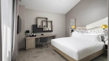 Una habitación de hotel moderna con tragaluz, una cama, un escritorio con silla y una mesita de noche con lámpara.