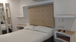 Een slaapkamer met een bed, nachtkastje, ingebouwd hoofdbord en een plank met een afstandsbediening.