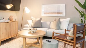 Een moderne woonkamer met een bank, een rond bijzettafeltje, een houten kast, een vloerlamp en een ingelijst kunstwerk aan de muur.