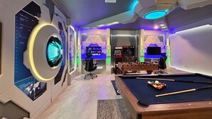 Una sala de juegos moderna con mesa de billar, consolas de videojuegos y un diseño futurista.