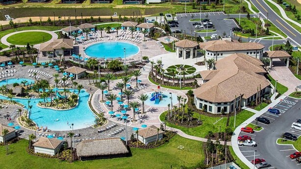 Vista aérea de un complejo turístico con varias piscinas, una piscina circular central y un aparcamiento.