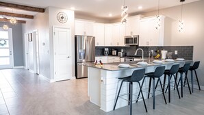 Una cocina moderna con armarios blancos, una isla grande con taburetes de bar, electrodomésticos de acero inoxidable e iluminación colgante.