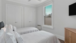 A bedroom with two beds, a ceiling fan, a window with a view, and a TV mounted on the wall.