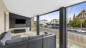 Un balcón con un sofá, un televisor de pantalla plana y vista a la calle y edificios.