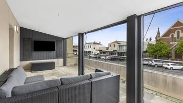 A balcony with a sofa, a flat-screen TV, and a view of the street and buildings.