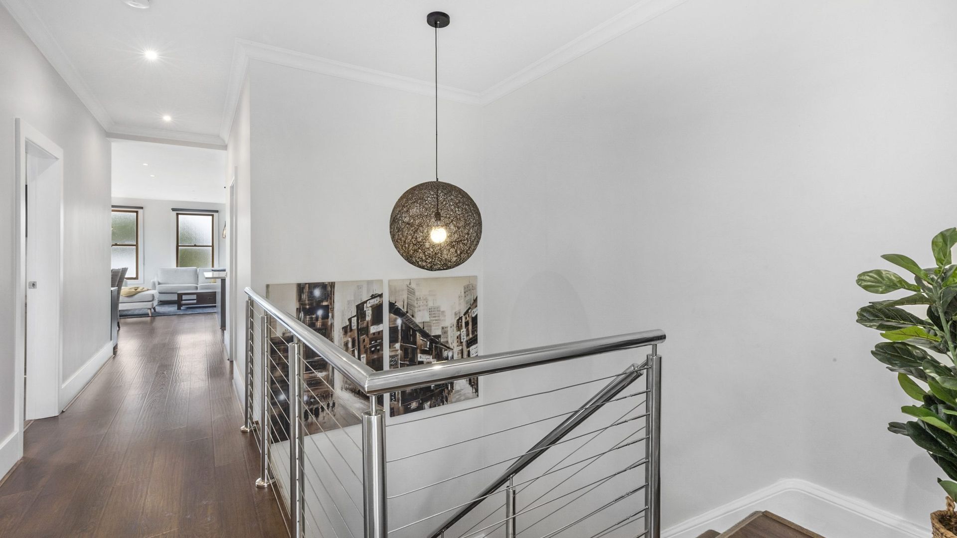 A modern interior with a staircase, a hanging light fixture, and a framed cityscape photo.