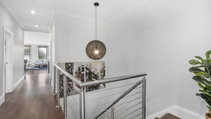 Un interior moderno con una escalera, una lámpara colgante y una fotografía enmarco de un paisaje urbano.