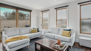Una sala de estar moderna con dos sofás grises, una mesa de centro de madera y ventanas amplias con persianas.