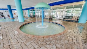 Ein Poolbereich mit einem zentralen Wasserspiel, gefliestem Boden und blauen Säulen.