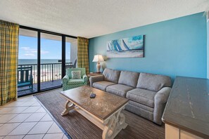 A room with a sofa, a green armchair, a coffee table, a lamp, and a painting on the wall. - NEW Upscale 1BR Direct Oceanfront with Amazing Views (Myrtle Beach)