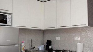Moderni keittiö, jossa on valkoiset kaapit, tumma työtaso, mikroaaltouuni, liesi ja riippuvalaisin.