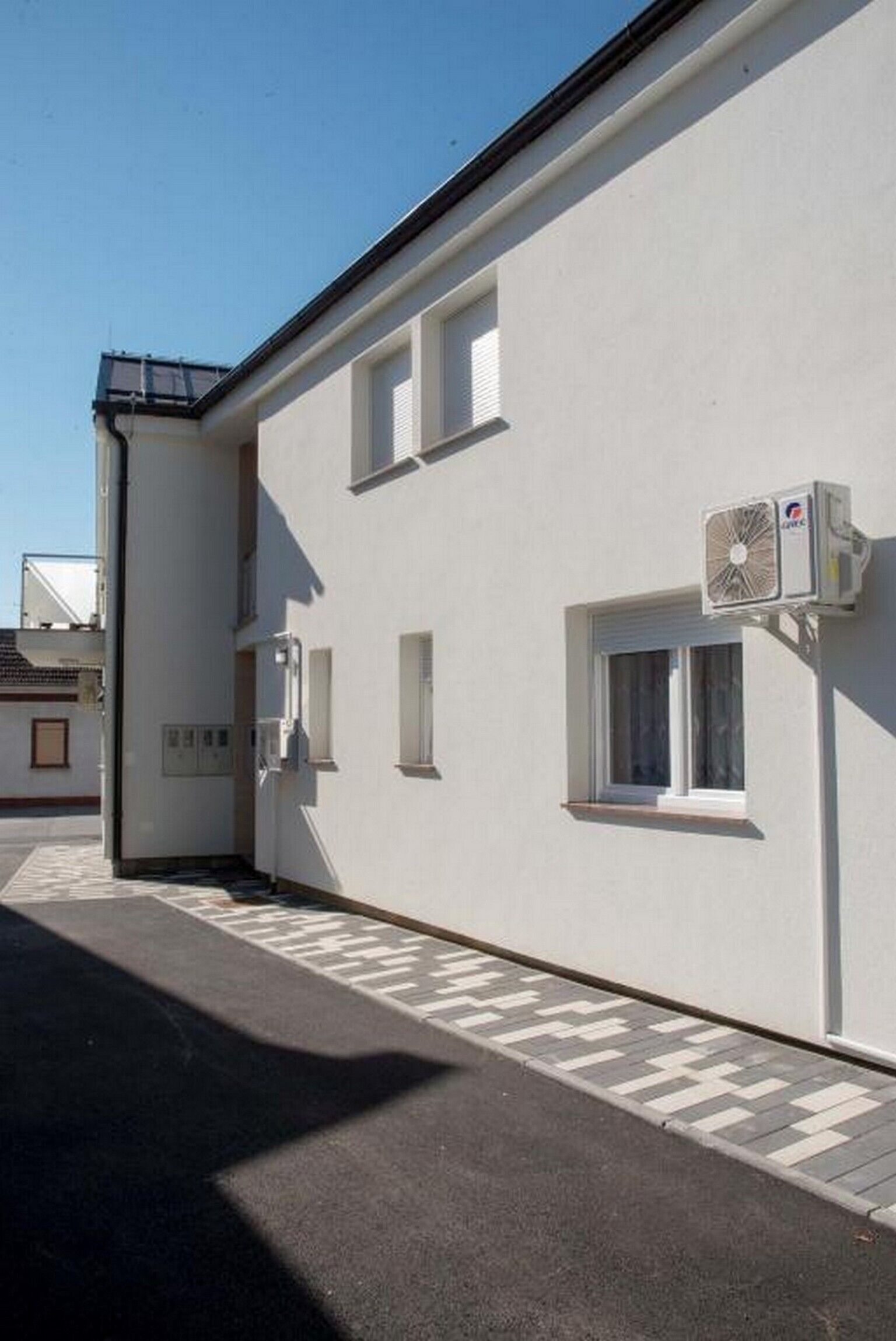 Un bâtiment blanc avec un toit plat, une petite fenêtre et un appareil de climatisation fixé au mur.