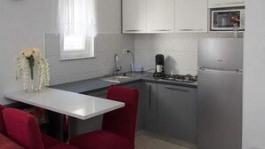 Une cuisine compacte avec des meubles blancs, un réfrigérateur en acier inoxydable, un four à micro-ondes et un évier. On y trouve une table à manger avec deux chaises rouges et un vase de fleurs.