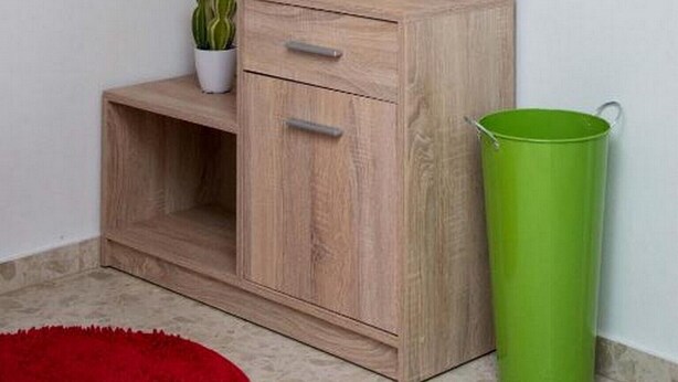 Une coiffeuse en bois avec un miroir, une petite étagère avec des fleurs, une plante en pot et une poubelle verte.