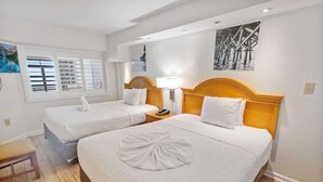 Une chambre d’hôtel avec deux lits, une tête de lit en bois, une table de chevet, une lampe et un tableau au mur.