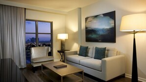 Une chambre d’hôtel moderne, dotée d’un canapé, d’un fauteuil et d’une table basse. Une grande fenêtre offre une vue sur la ville.