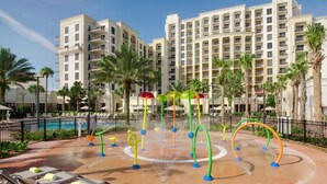 Une cour d’hôtel avec une piscine, des chaises longues et un espace de jeux aquatiques.