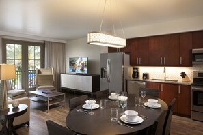 A modern kitchen with dark wooden cabinets, stainless steel appliances, and a dining area with a round table set for four. - Orlando | Park Escape | Pool & Attractions | 2BR Plus (Orlando)