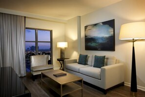 A modern hotel room with a sofa, armchair, and a coffee table. A large window offers a city view. - Orlando | Park Escape | Pool & Attractions | 2BR Plus (Orlando)