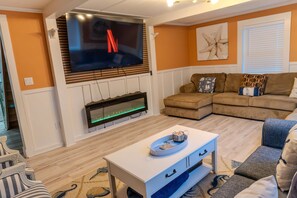 Ein Wohnzimmer mit Flachbildfernseher an der Wand, Kamin, Ecksofa und Couchtisch.