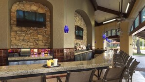 A bar area with stone walls, a flat-screen TV, and a long counter with bar stools. - Orlando | Couples Resort Stay | Pool + Hot Tub (Orlando)