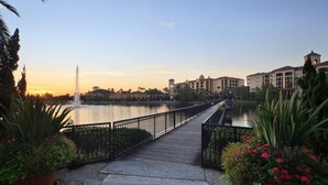 A waterfront promenade with a wooden walkway, a fountain, and buildings in the background. - Orlando | Couples Resort Stay | Pool + Hot Tub (Orlando)
