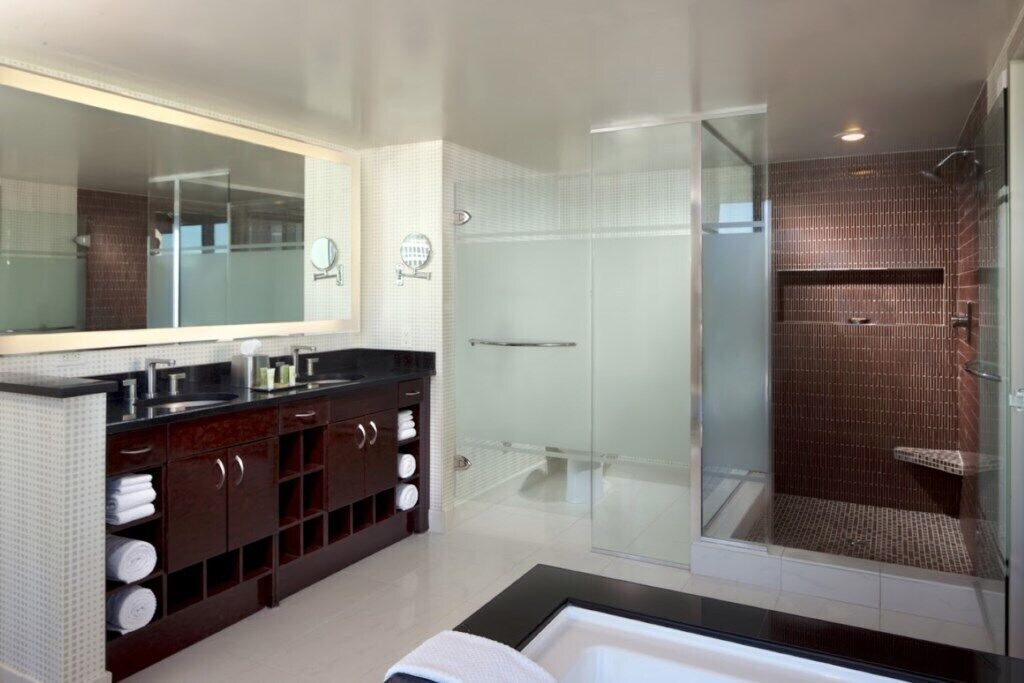 Un baño moderno con un espejo grande, tocador de madera oscura y cabina de ducha con mampara de vidrio.