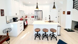 A modern kitchen with white cabinets, a stainless steel refrigerator, a central island with stools, pendant lighting, and a black fan. - Local Host: 3BR 2.5BA by BSU DT GreenBelt & Skiing (Boise)