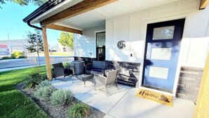 A covered outdoor seating area with a patio table and chairs, a small fire pit, and a door with a 'Home' sign. - Local Host: 3BR 2.5BA by BSU DT GreenBelt & Skiing (Boise)