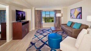 A hotel room with a television, a sofa, a coffee table, a lamp, and a window with a view. - Paradise, a Hilton Grand Vacations Club - 1 Bedroom - EP (Las Vegas)