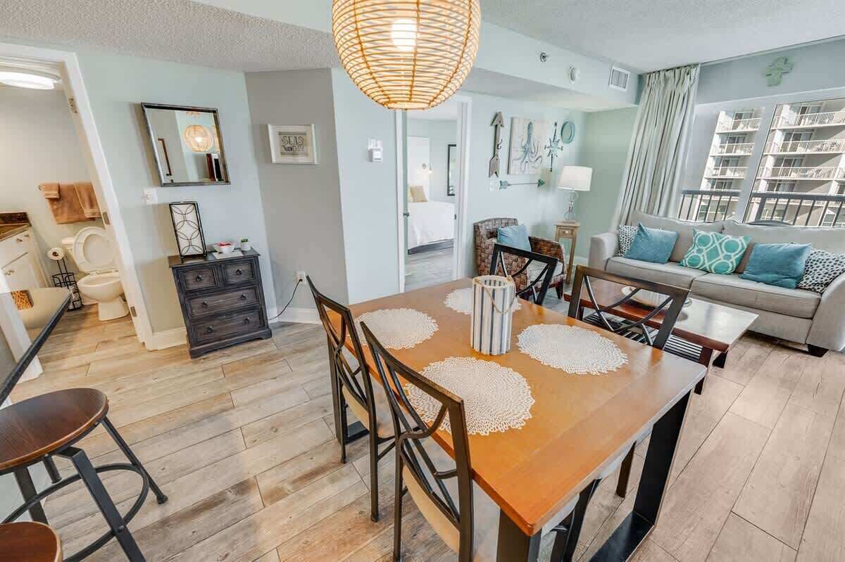 Uma sala de estar moderna com uma mesa de jantar de madeira, um sofá e uma janela grande com vista para um edifício.