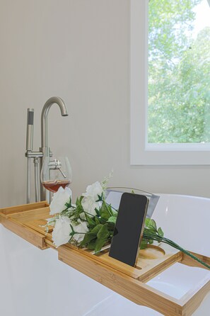 Een badkamer met een houten dienblad waarop een smartphone, een glas rode wijn en witte bloemen staan.