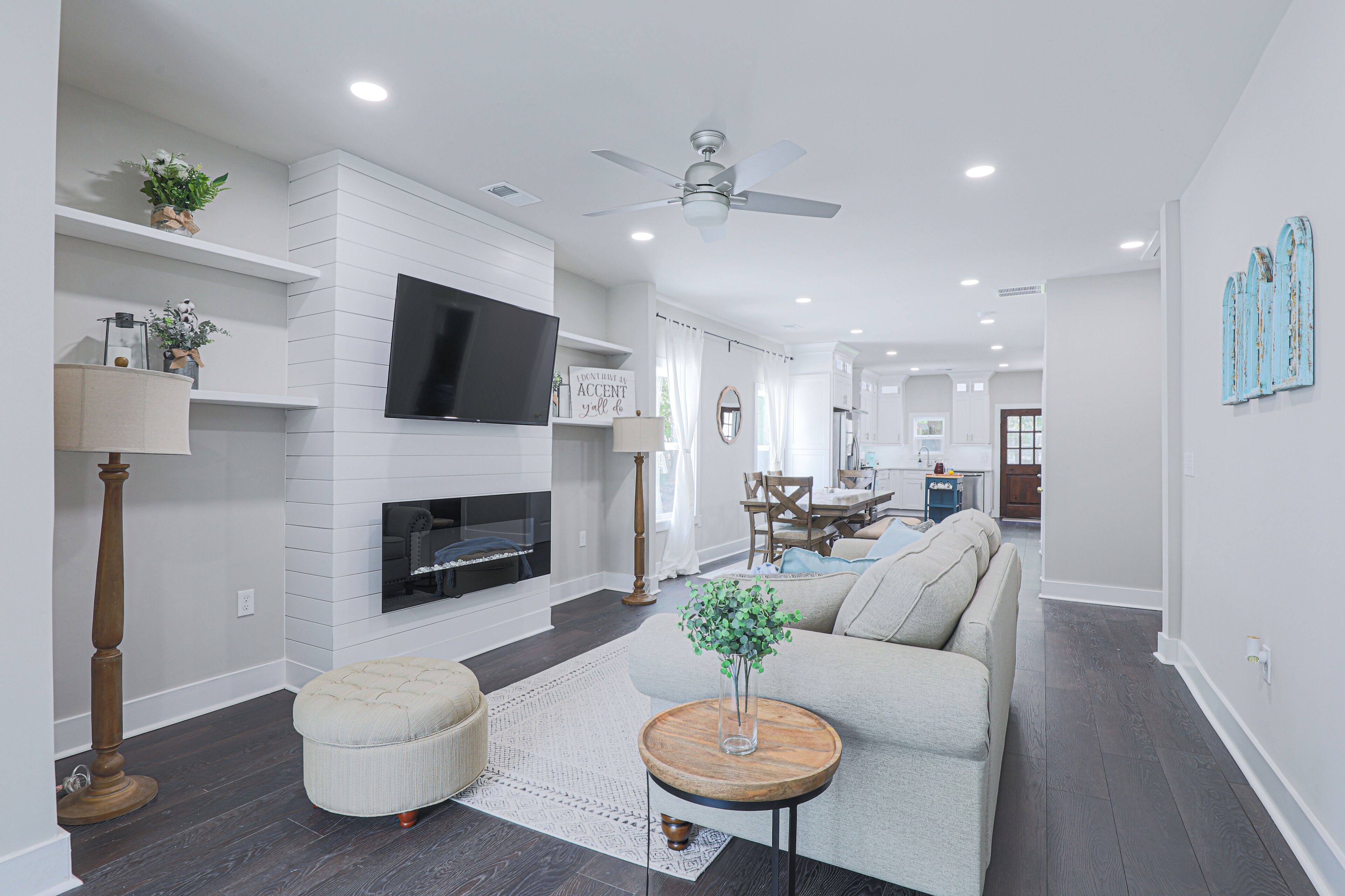 A modern living room with a flat-screen TV, a fireplace, a dining area, and a kitchen in the background.