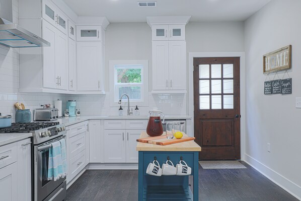 A kitchen with white cabinets, a stove, a sink, and a wooden door.