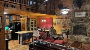 A rustic interior with a wooden staircase, a stone fireplace, a dining area, and a leather sofa.